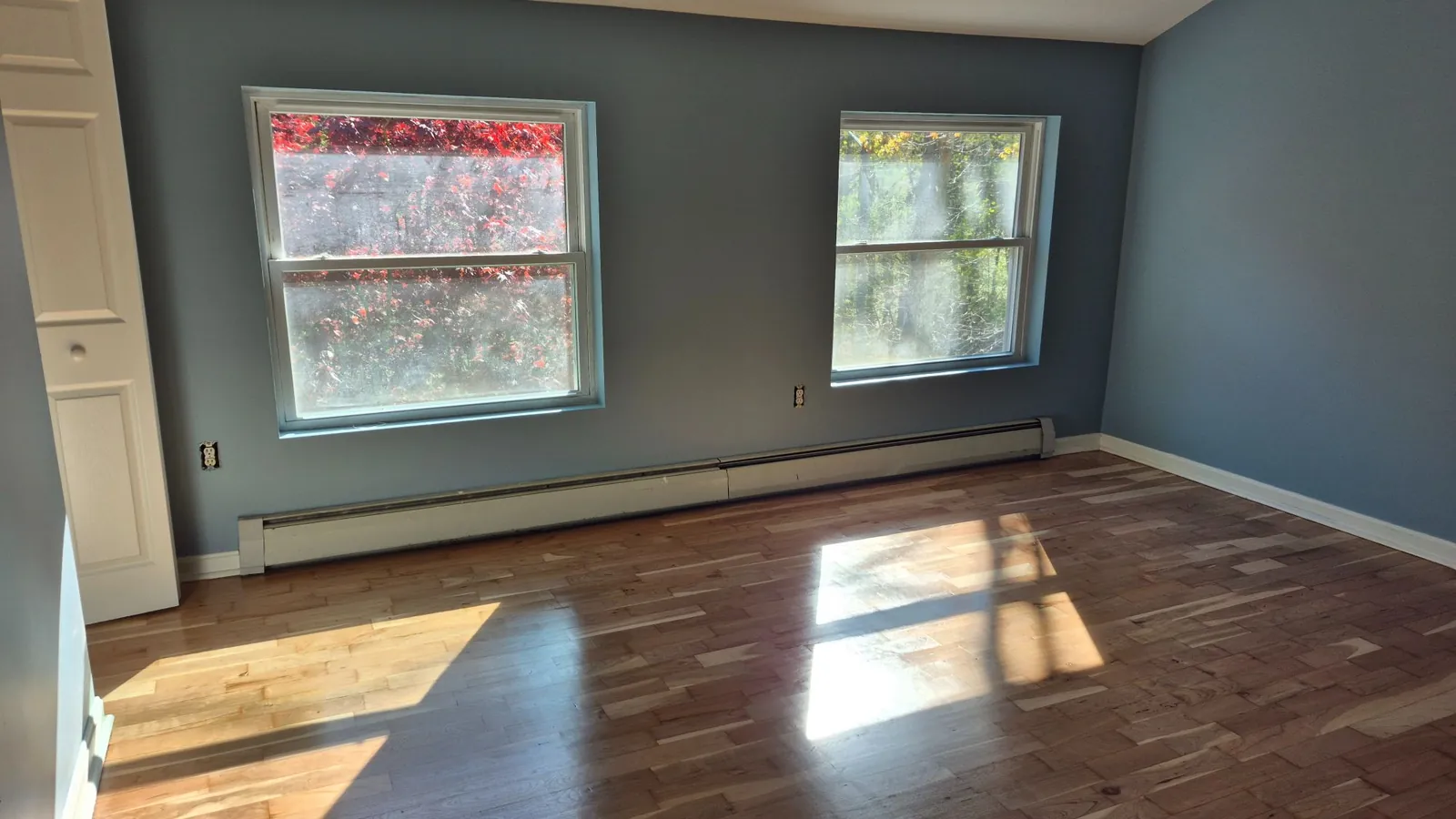 A freshly painted bedroom with blue walls, white trim and hardwood floors